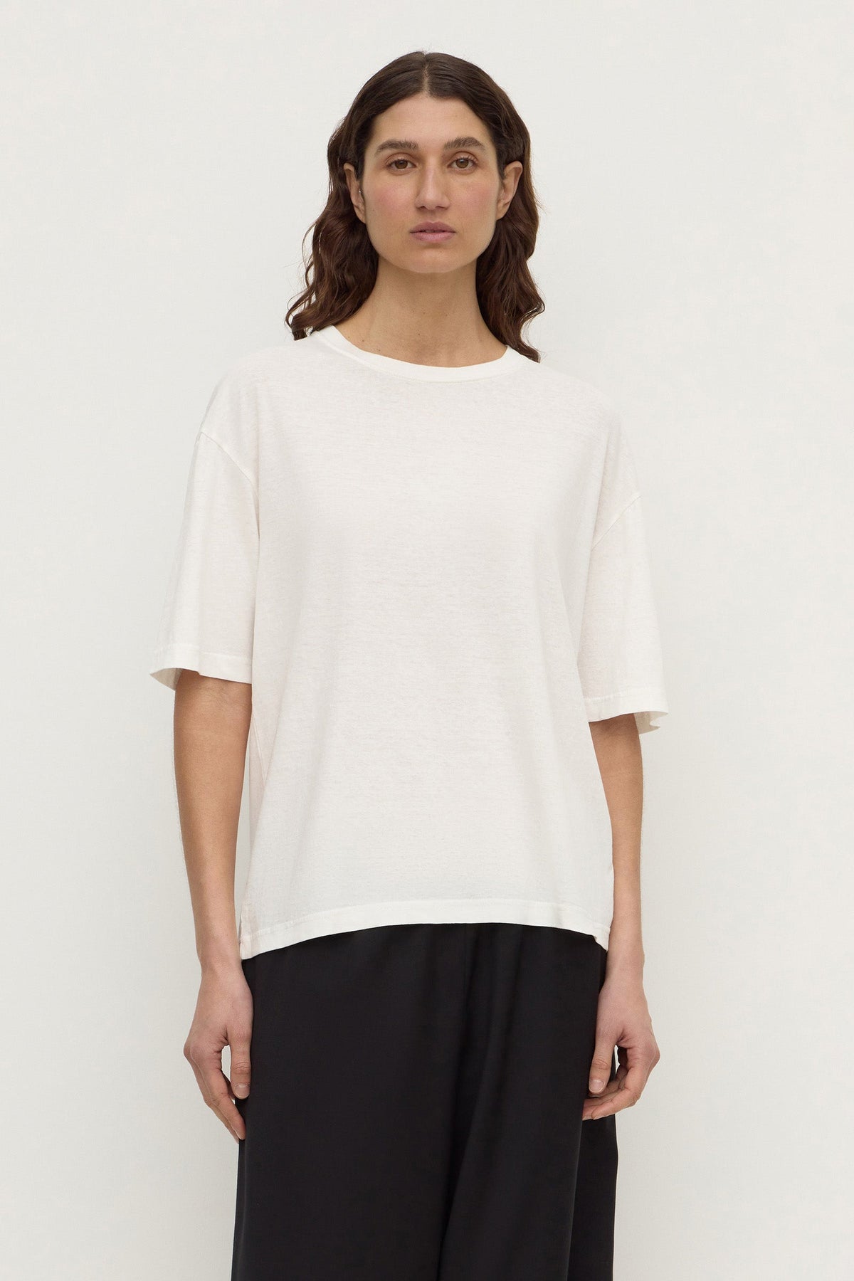 A woman wearing an antique white short-sleeve tee with a ribbed crew neckline and relaxed boxy fit, shown from the front.