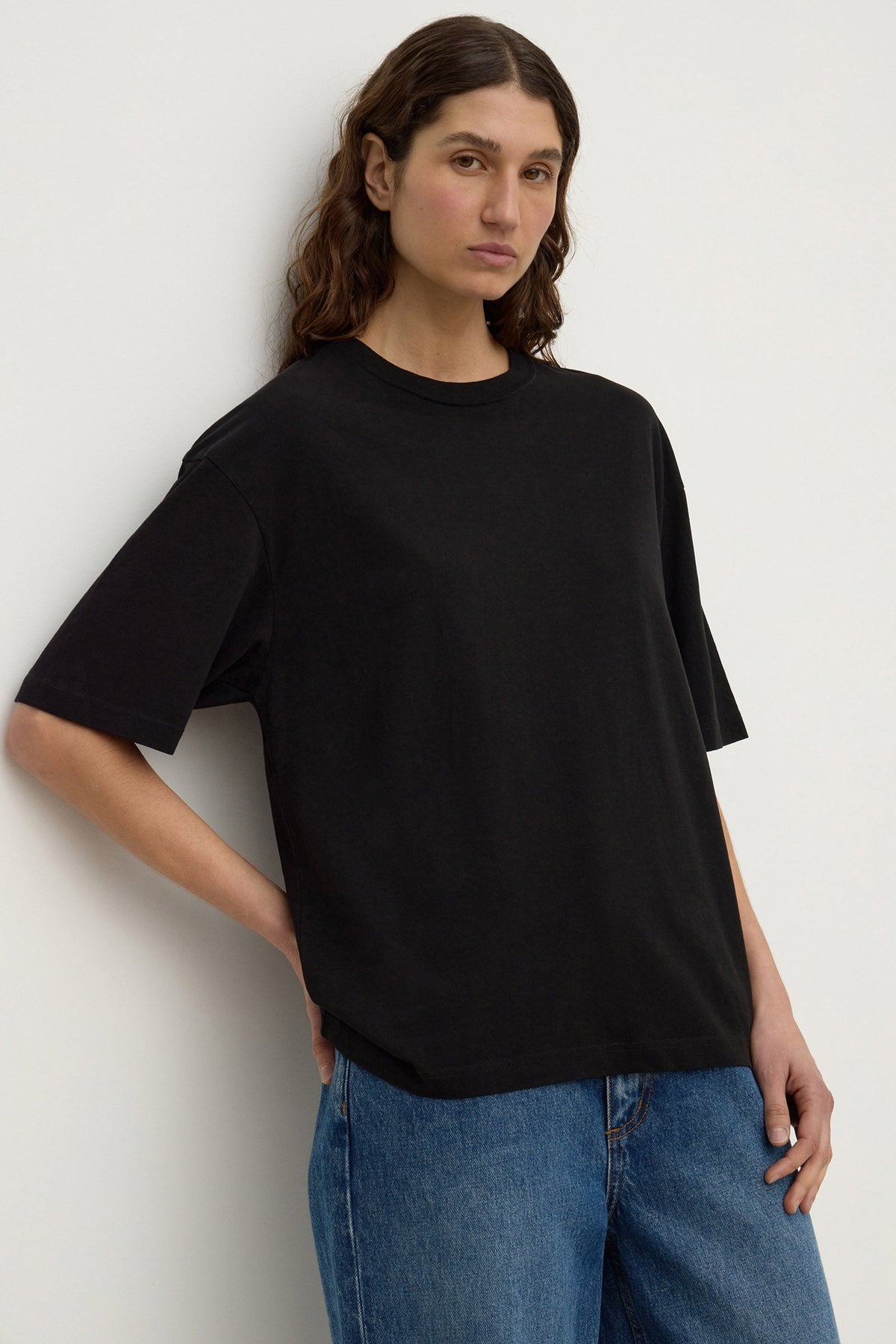 Black tee shown from a three-quarter angle, highlighting the ribbed neckline, dropped shoulders and relaxed silhouette.