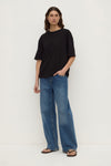 Full-length front view of a model wearing a black oversized short-sleeve tee with blue wide-leg jeans.