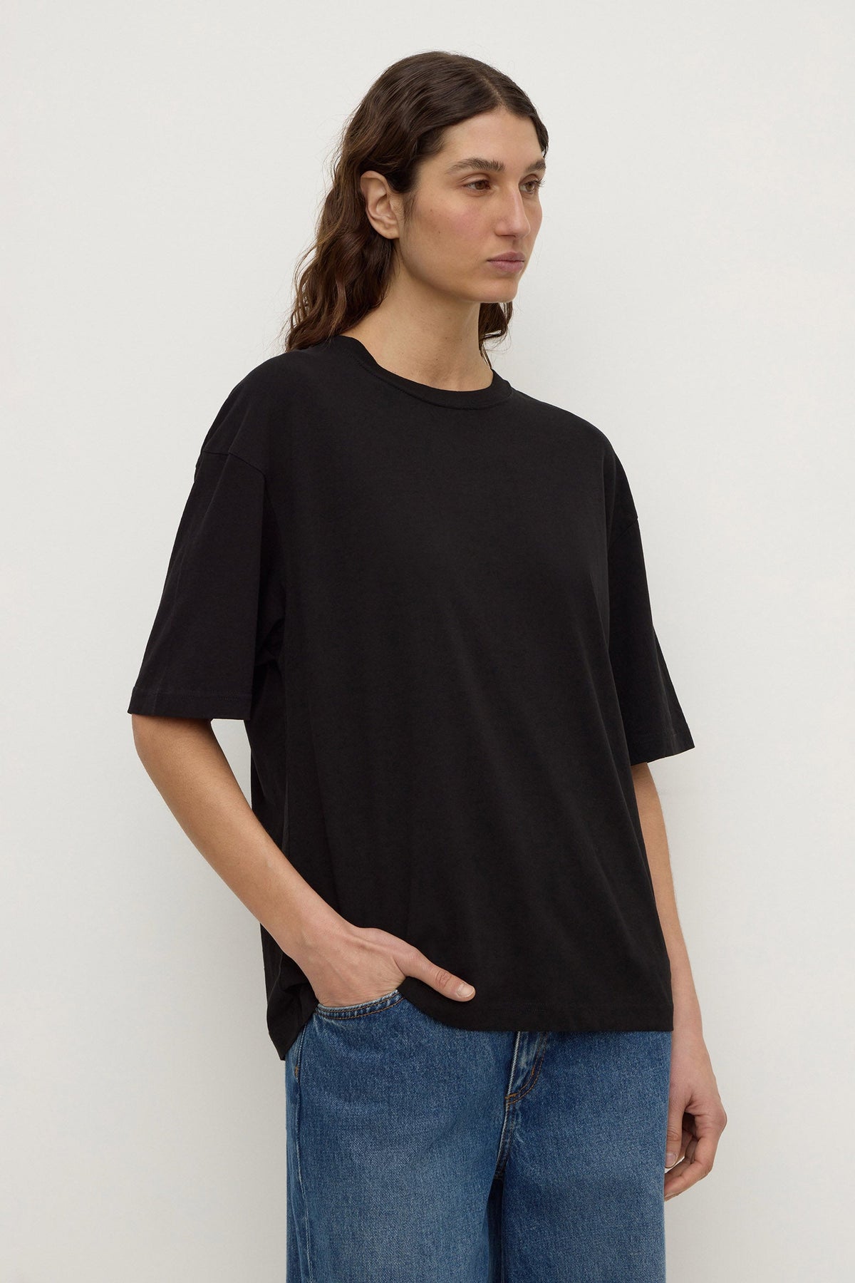 Three-quarter view of a black short-sleeve tee with a straight hem and relaxed fit, paired with blue denim.