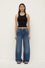 Person wearing a black tank top and blue jeans on a white background