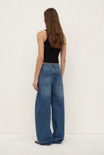 Woman wearing blue jeans and a black top on a white background