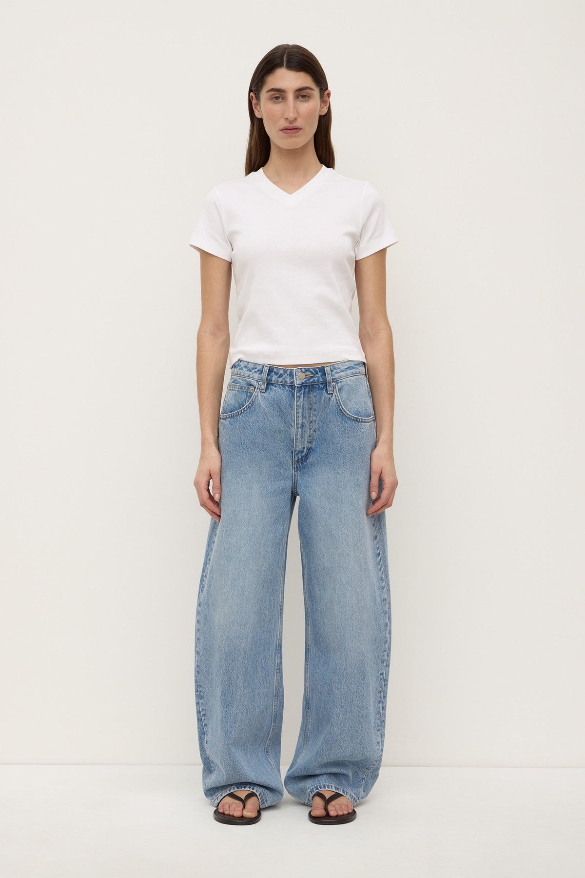 A model wearing indigo fade mid-rise relaxed jeans with wide legs, five-pocket construction and curved outer seams that taper towards the hems, shown from the front.