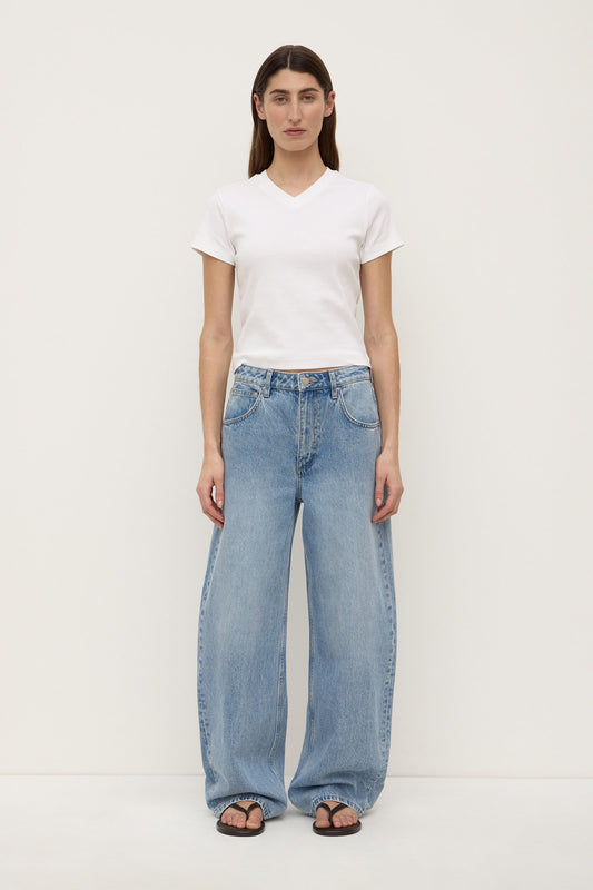 A model wearing indigo fade mid-rise relaxed jeans with wide legs, five-pocket construction and curved outer seams that taper towards the hems, shown from the front.