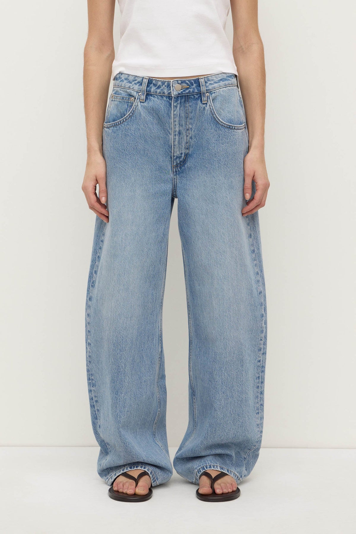 Close-up front view of indigo fade jeans showing the mid-rise waistband, button and zip fly, belt loops, curved front pockets and wide-leg shape.