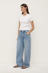 A model wearing indigo fade relaxed jeans from a three-quarter angle, showing the wide legs, mid-rise waist and curved outer seams.