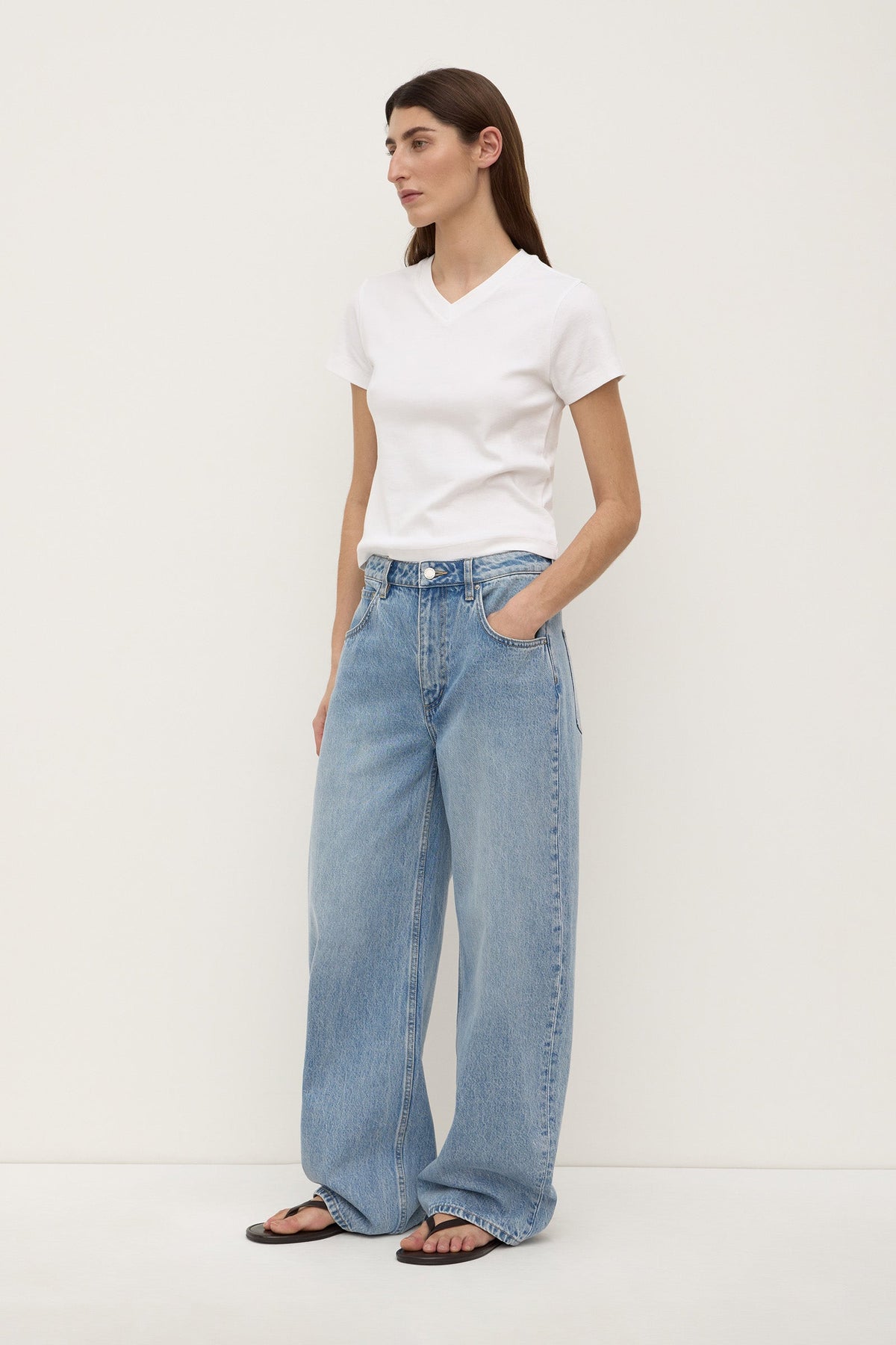 A model wearing indigo fade relaxed jeans from a three-quarter angle, showing the wide legs, mid-rise waist and curved outer seams.