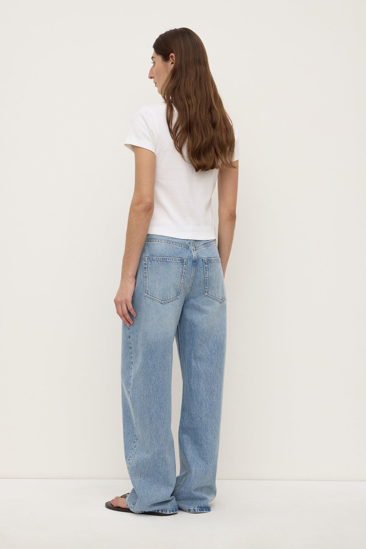 Back view of a model wearing indigo fade relaxed jeans, showing the mid-rise waistband, belt loops, back patch pockets and wide-leg silhouette.