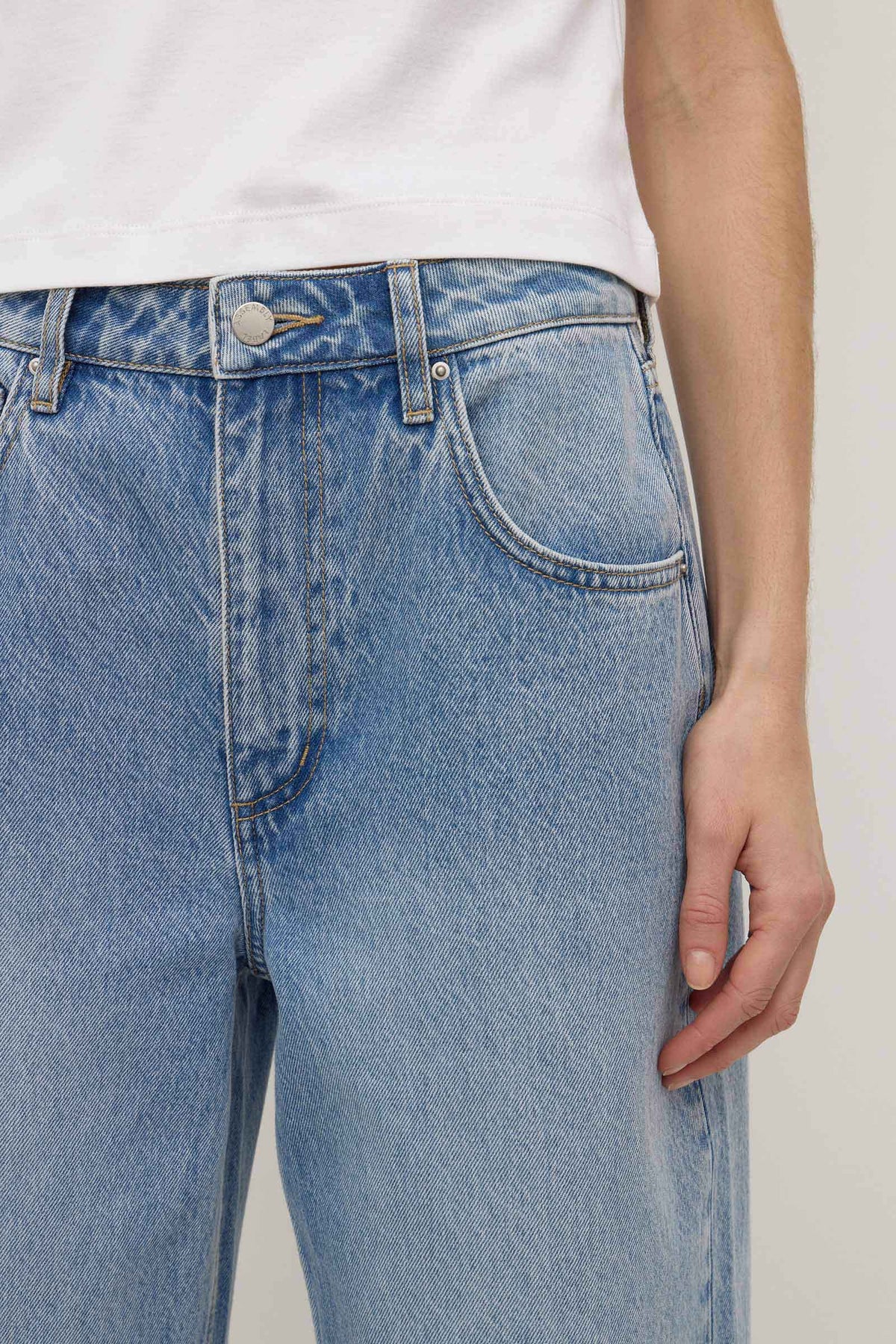 Close-up of the indigo fade jeans showing the waistband, metal button, belt loop, zip fly and curved front pocket stitching.