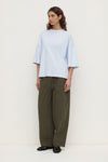 Model wearing a powder blue oversized short-sleeve tee with olive wide-leg trousers and black shoes, full-length front view