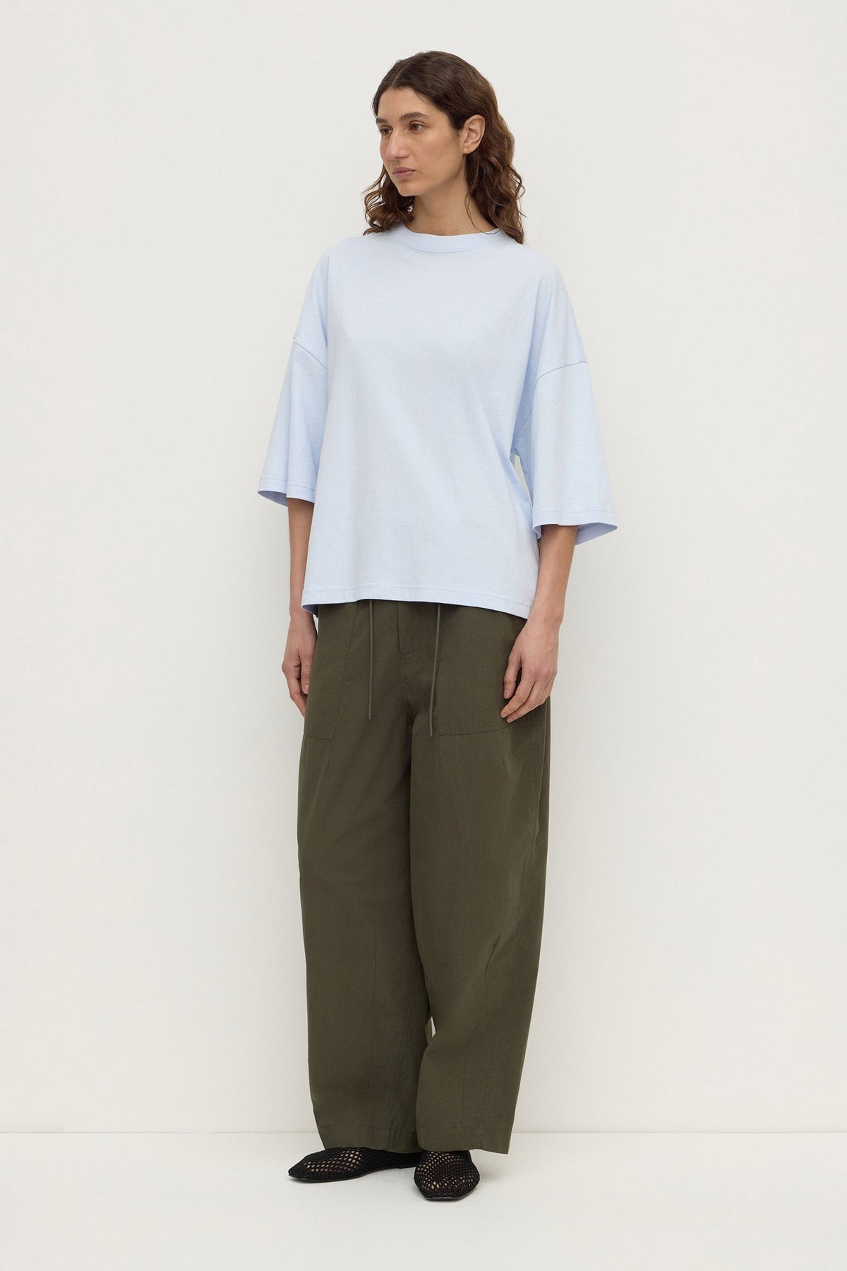 Model wearing a powder blue oversized short-sleeve tee with olive wide-leg trousers and black shoes, full-length front view