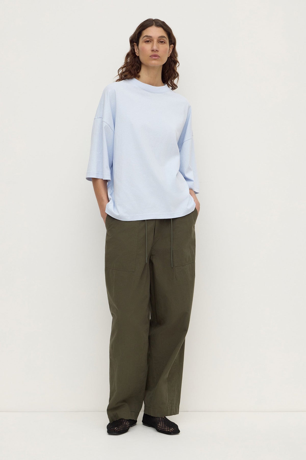 Model wearing a powder blue oversized short-sleeve tee with olive trousers, showing the relaxed fit and wide sleeves, full-length front view