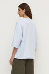 Model wearing a powder blue oversized short-sleeve tee with olive trousers, showing the dropped shoulders, wide sleeves and relaxed silhouette, back view