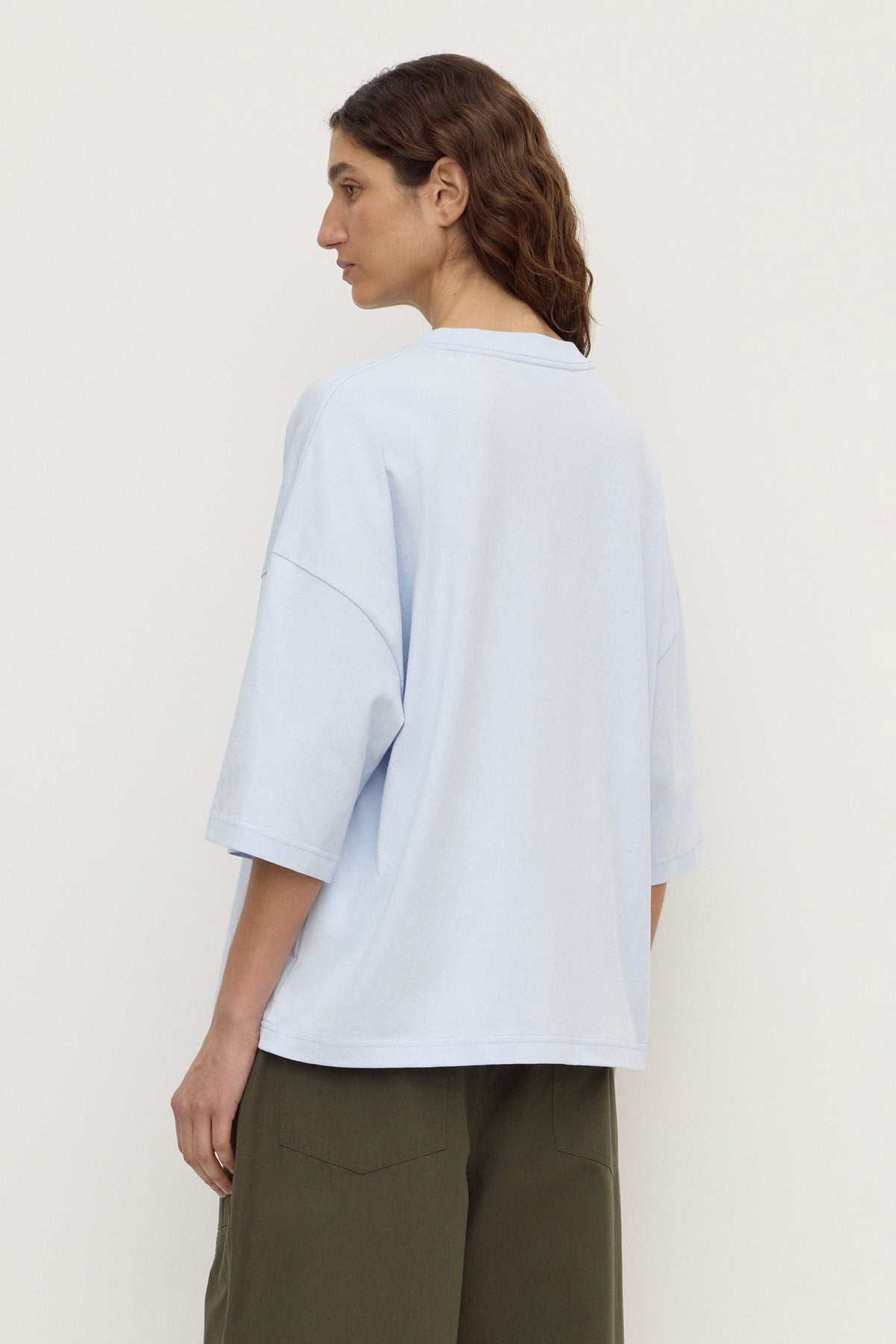 Model wearing a powder blue oversized short-sleeve tee with olive trousers, showing the dropped shoulders, wide sleeves and relaxed silhouette, back view