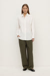 Model wearing a white long-sleeve button-up shirt with olive trousers and black shoes, showing the relaxed silhouette and button-front design, full-length front view