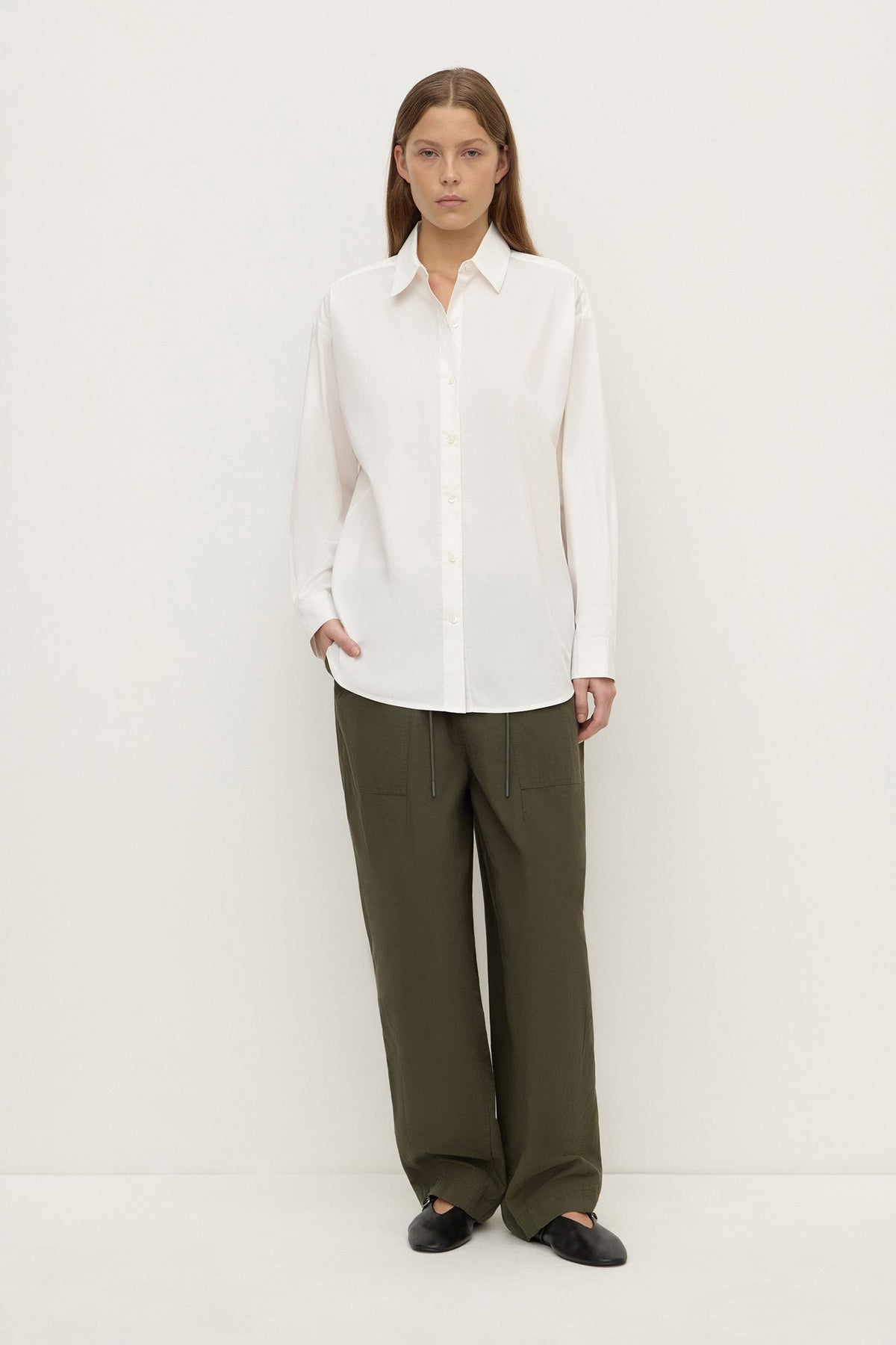 Model wearing a white long-sleeve button-up shirt with olive trousers and black shoes, showing the relaxed silhouette and button-front design, full-length front view