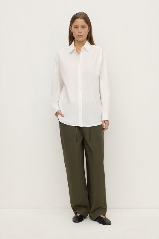 Model wearing a white long-sleeve button-up shirt with olive trousers and black shoes, showing the relaxed silhouette and button-front design, full-length front view