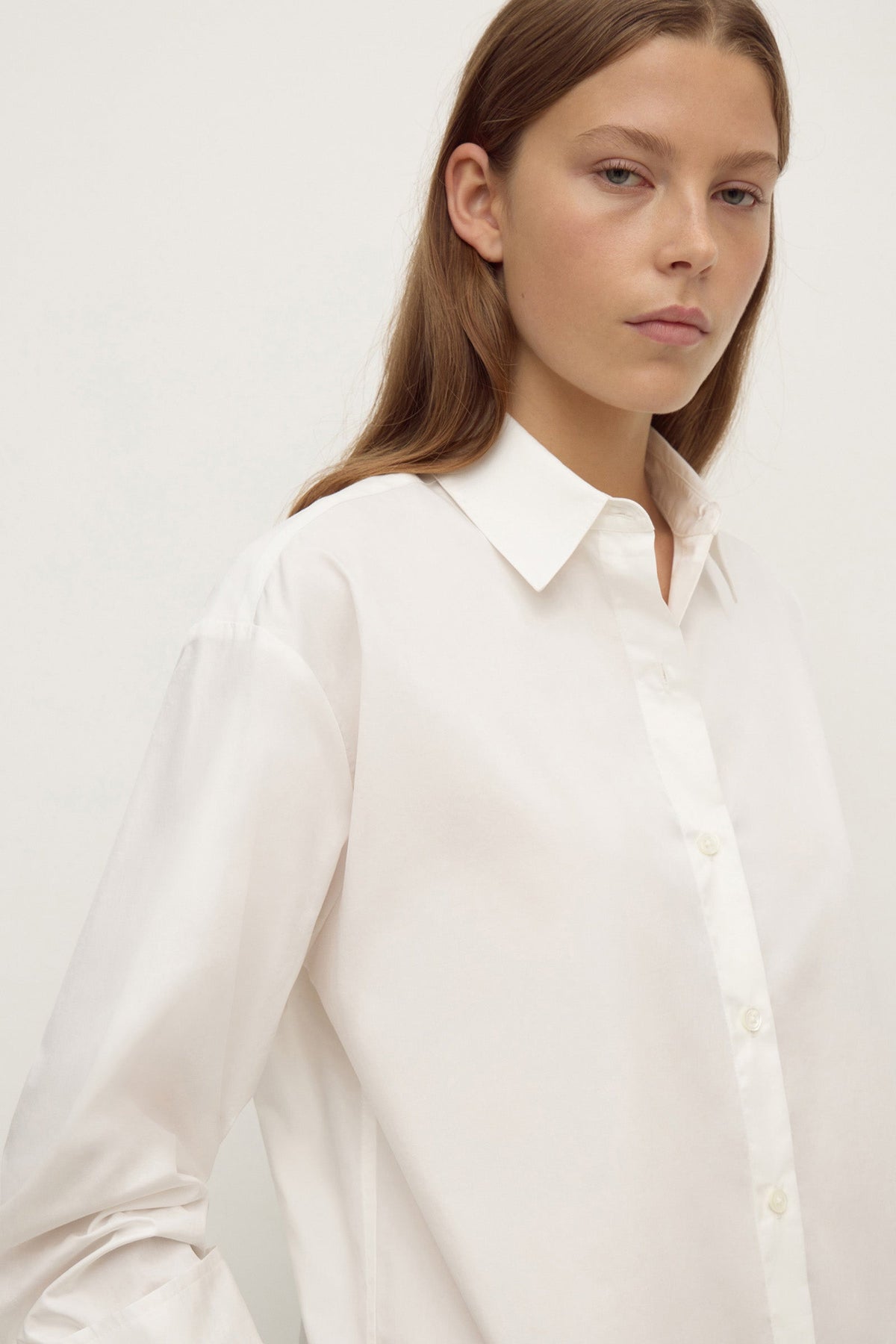 Close-up of model wearing a white long-sleeve button-up shirt, showing the pointed collar, front buttons and relaxed shoulder fit