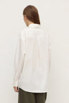 Model wearing a white long-sleeve button-up shirt with olive trousers, showing the back yoke, long sleeves and curved hem, back view
