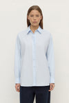 Model wearing a powder blue long-sleeve button-up shirt with navy trousers, showing the pointed collar, button front and relaxed fit, front view
