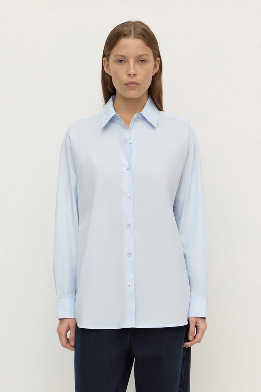 Model wearing a powder blue long-sleeve button-up shirt with navy trousers, showing the pointed collar, button front and relaxed fit, front view