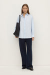 Model wearing a powder blue long-sleeve button-up shirt with navy wide-leg trousers and a black shoulder bag, full-length front view