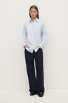 Model wearing a powder blue long-sleeve button-up shirt with navy wide-leg trousers, showing the curved hem and relaxed silhouette, front view