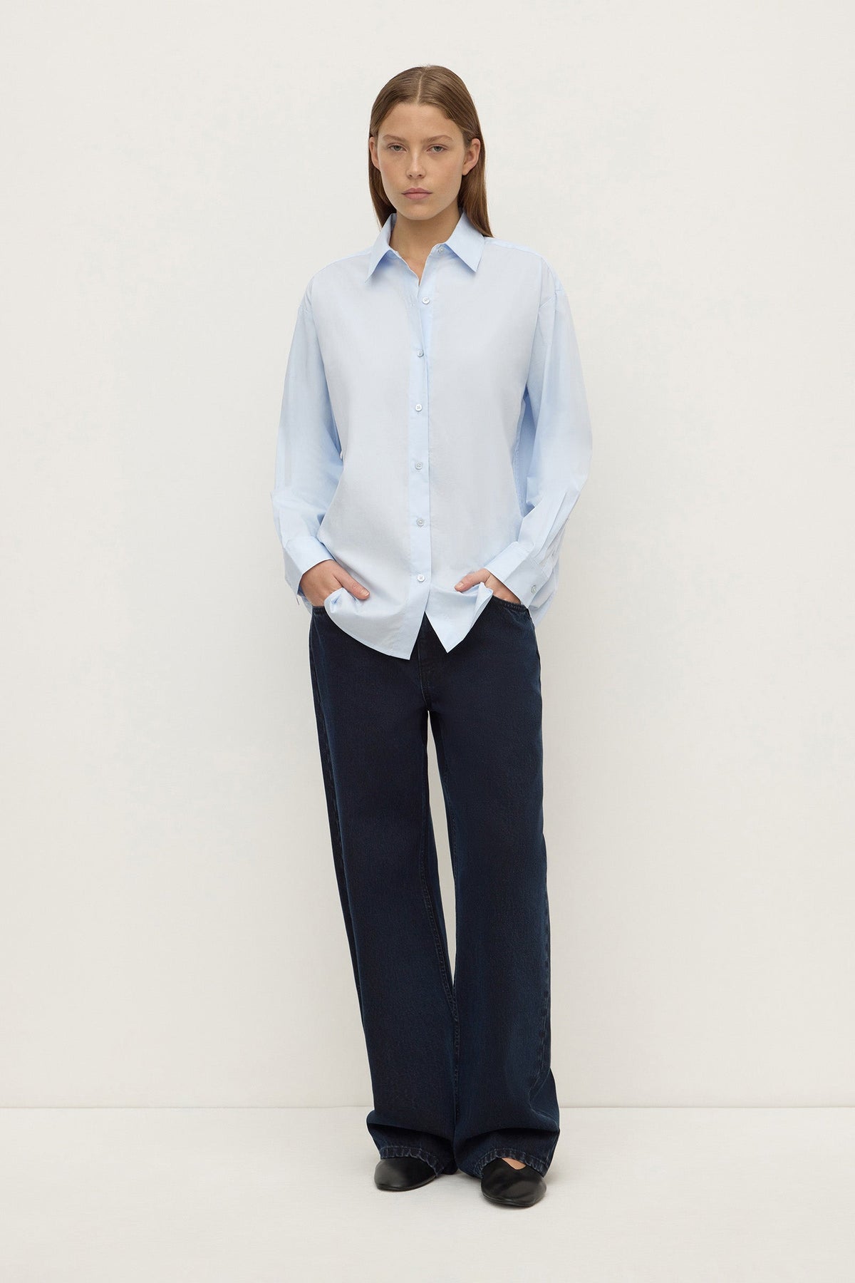 Model wearing a powder blue long-sleeve button-up shirt with navy wide-leg trousers, showing the curved hem and relaxed silhouette, front view