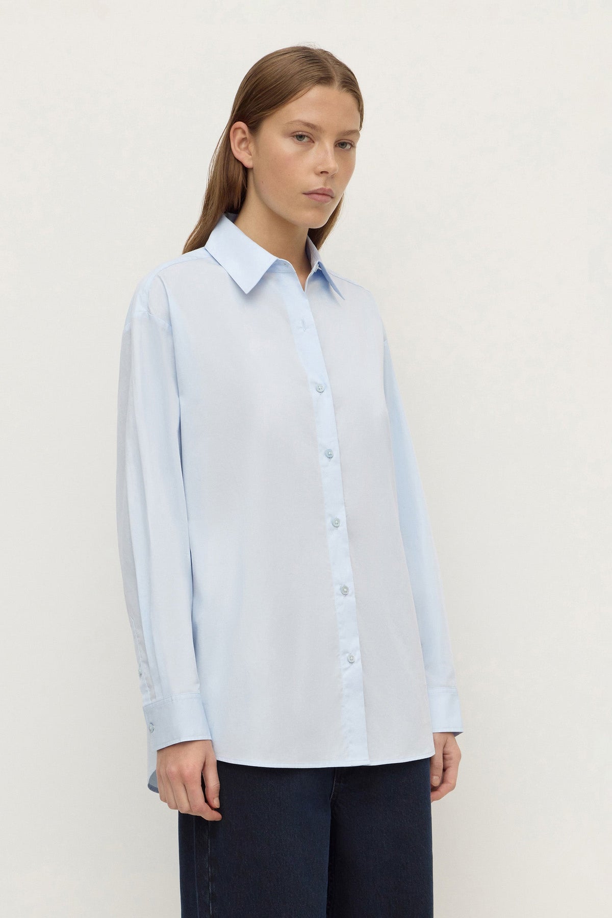 Model wearing a powder blue long-sleeve button-up shirt with navy trousers, showing the pointed collar, long sleeves and relaxed fit, angled front view