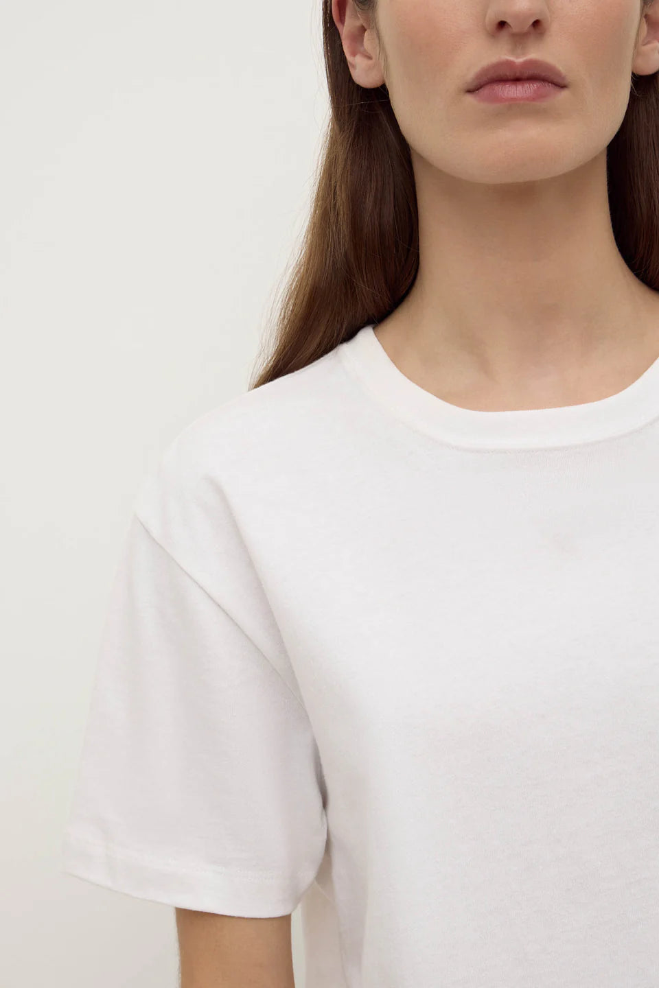 Close-up of the white tee, showing the classic crew neckline, short sleeves, smooth cotton jersey and clean minimal finish, front detail view
