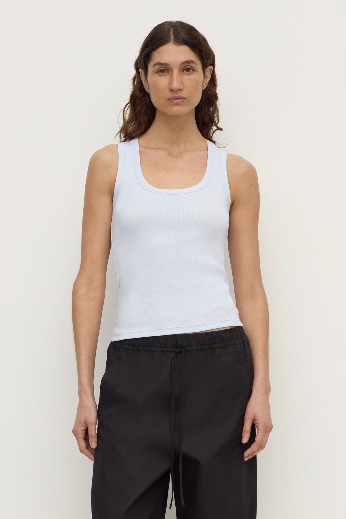 Model wearing a powder blue fitted rib tank with black trousers, showing the scoop neckline and sleeveless silhouette, front view