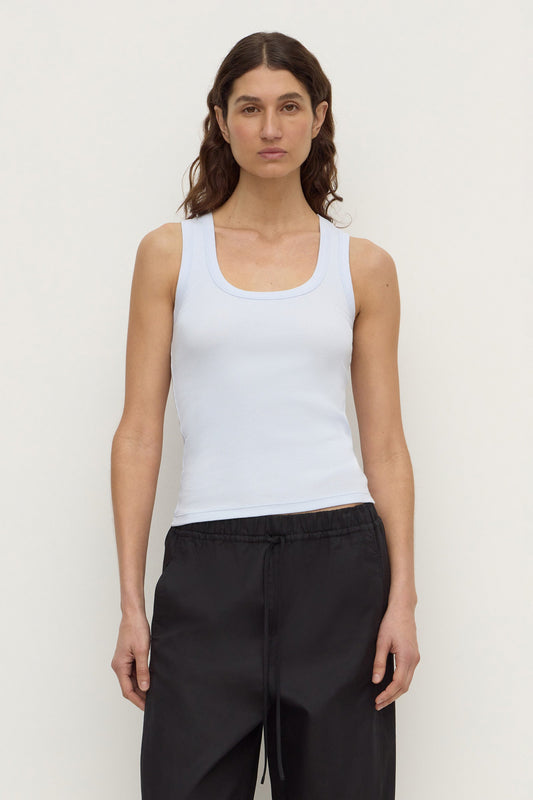 Model wearing a powder blue fitted rib tank with black trousers, showing the scoop neckline and sleeveless silhouette, front view