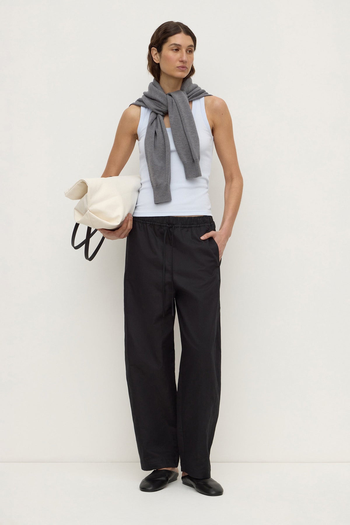 Model wearing a powder blue fitted rib tank with black wide-leg trousers, grey knit draped over the shoulders and a white bag, full-length front view