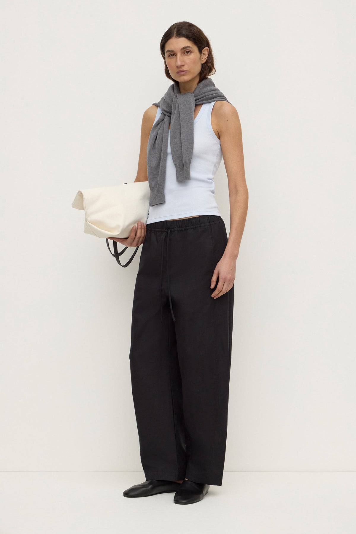 Model wearing a powder blue fitted rib tank with black wide-leg trousers, grey knit draped over the shoulders and a white bag, angled front view