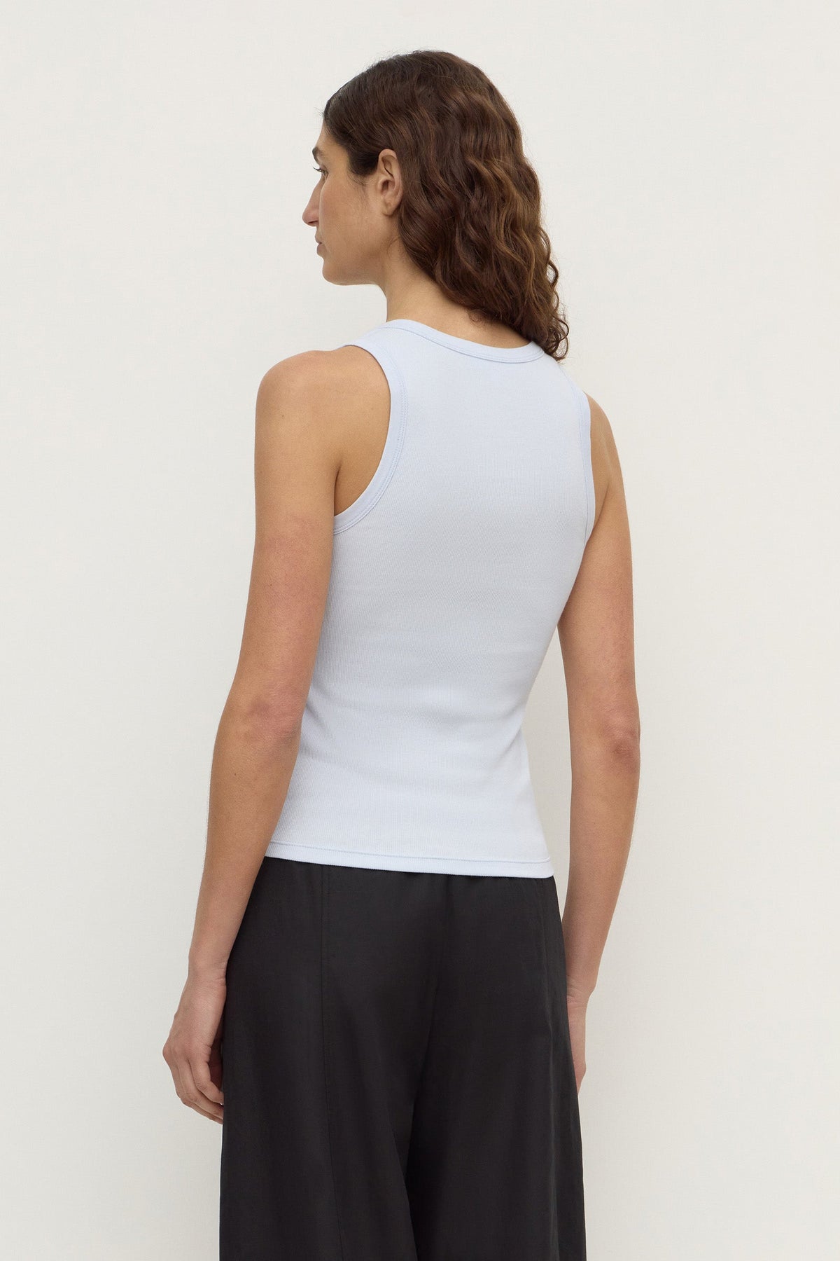 Model wearing a powder blue fitted rib tank with black trousers, showing the sleeveless cut and fitted back, back view
