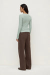 Woman wearing a light green sweater and brown pants on a white background