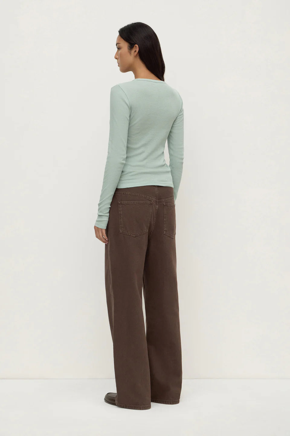 Woman wearing a light green sweater and brown pants on a white background
