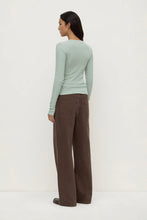 Woman wearing a light green sweater and brown pants on a white background