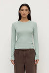 Woman wearing a light green long-sleeve top and brown pants on a white background