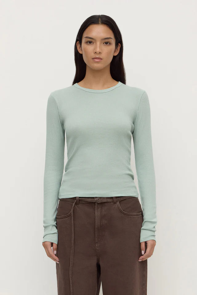 Woman wearing a light green long-sleeve top and brown pants on a white background