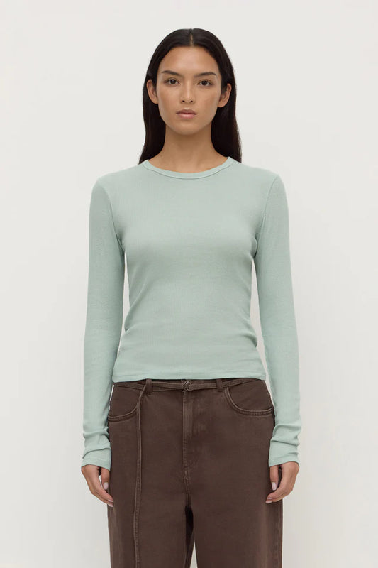 Woman wearing a light green long-sleeve top and brown pants on a white background