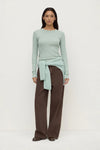 Woman wearing a light green sweater and brown pants on a white background