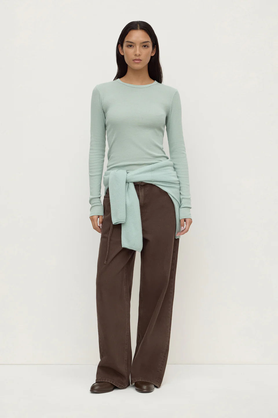 Woman wearing a light green sweater and brown pants on a white background