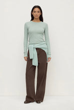 Woman wearing a light green sweater and brown pants on a white background