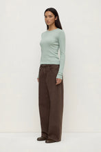 Woman wearing a light green sweater and brown pants on a white background