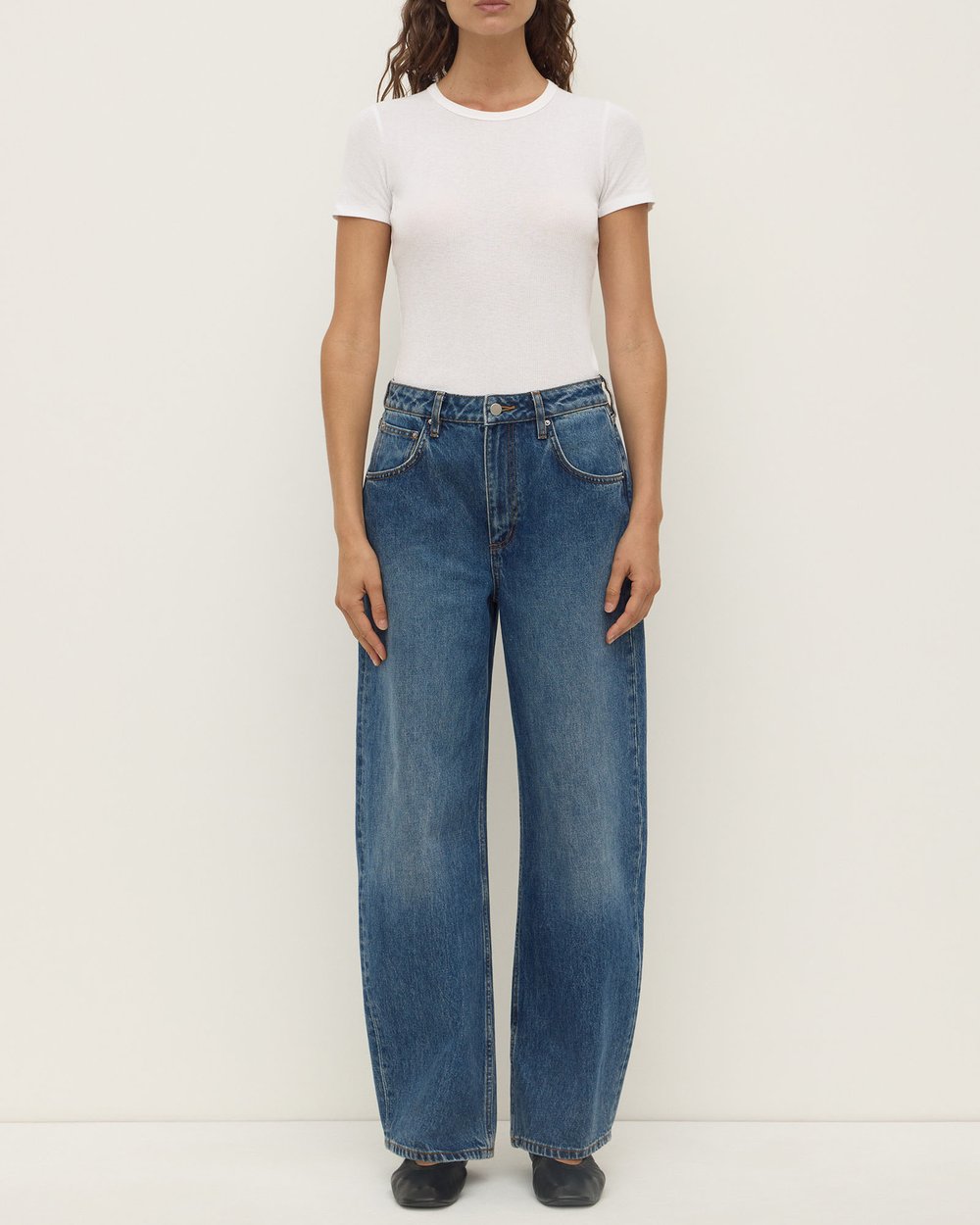 Model wearing the white Zali Short Sleeve Tee with relaxed blue jeans and black flats, showing the crew neckline, fitted short sleeves and close-to-body silhouette, full-length front view
