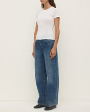 Model wearing the white short-sleeve tee with blue jeans and black flats, showing the fitted shape, crew neckline, ribbed texture and hip-length finish, angled front view
