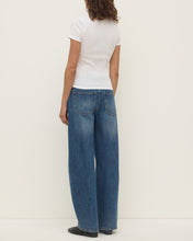Model wearing the white short-sleeve tee with blue jeans, showing the fitted back, short sleeves, clean neckline and straight hip-length hem, back view