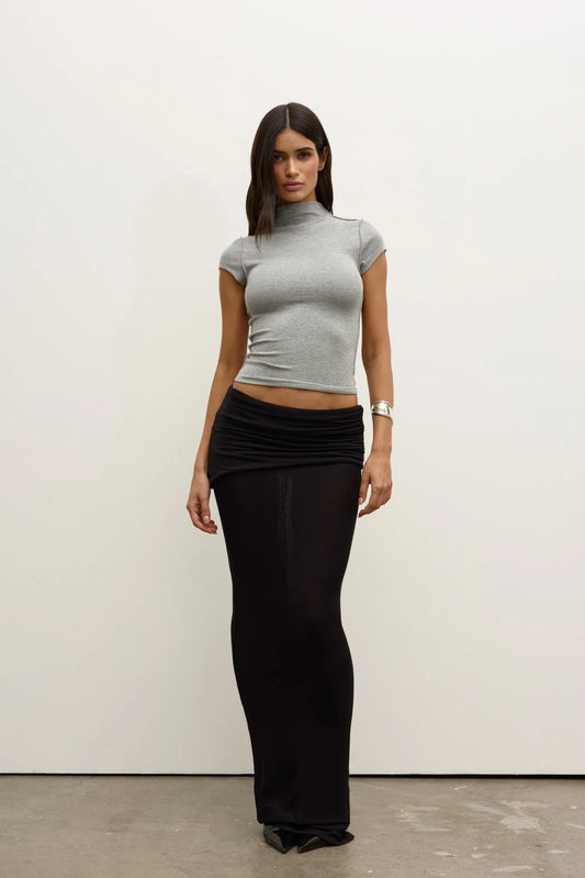 Model wearing a Grey Marle fitted cap-sleeve mock-neck top with a black ruched maxi skirt and pointed shoes, showing the cropped length and slim silhouette, front view