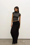 Woman wearing a gray top and black skirt against a white wall